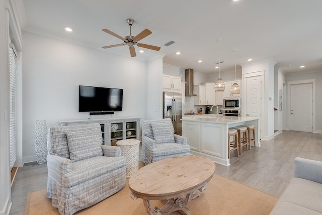 living room featuring ceiling fan, crown molding, light wood-type flooring, and sink