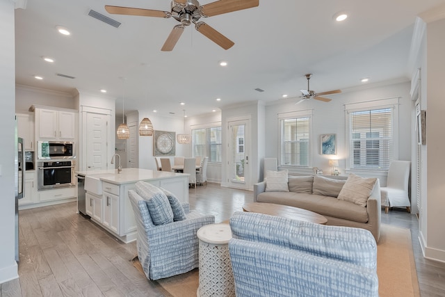 living room with sink, ornamental molding, light wood-type flooring, and ceiling fan