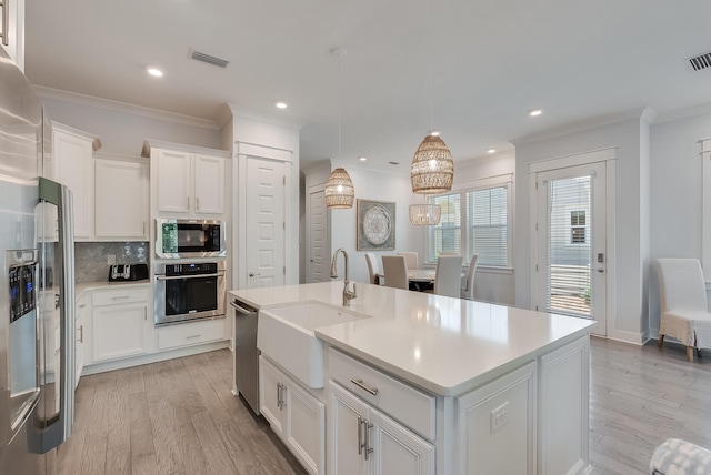 kitchen with appliances with stainless steel finishes, white cabinetry, pendant lighting, and a kitchen island with sink