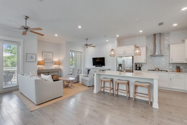 kitchen with wall chimney range hood, ceiling fan, stainless steel appliances, and a kitchen island with sink