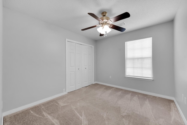 unfurnished bedroom featuring a textured ceiling, ceiling fan, light carpet, and a closet