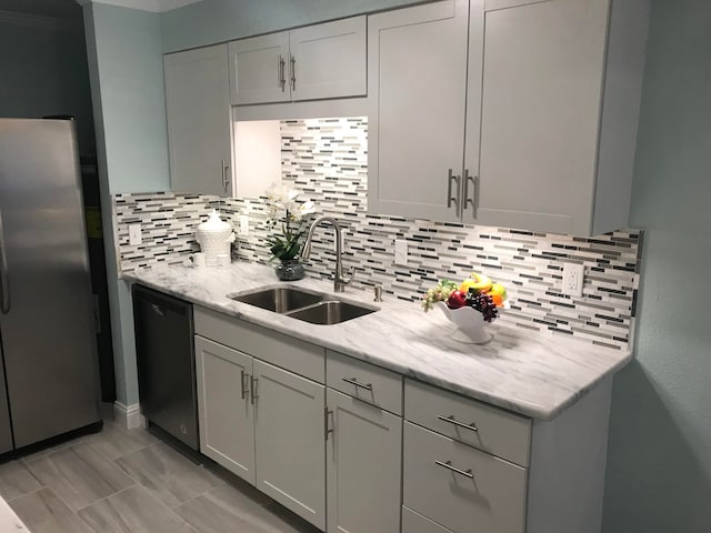 kitchen with dishwasher, sink, tasteful backsplash, light stone counters, and stainless steel refrigerator