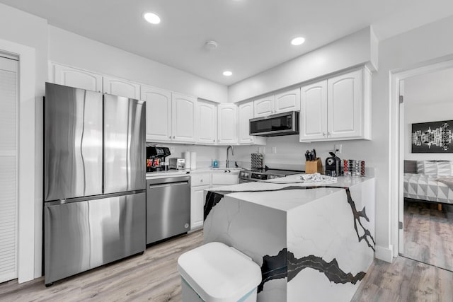 kitchen with light stone countertops, light wood-type flooring, white cabinetry, appliances with stainless steel finishes, and a sink
