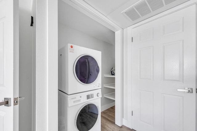 washroom featuring stacked washer and dryer, visible vents, wood finished floors, and laundry area