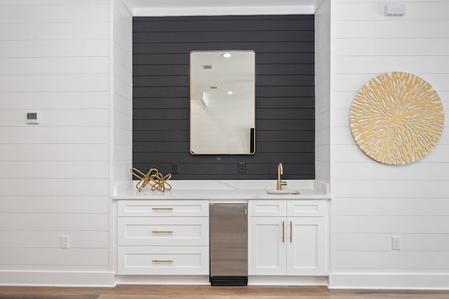 bar featuring white cabinets, light hardwood / wood-style flooring, wooden walls, and light stone counters