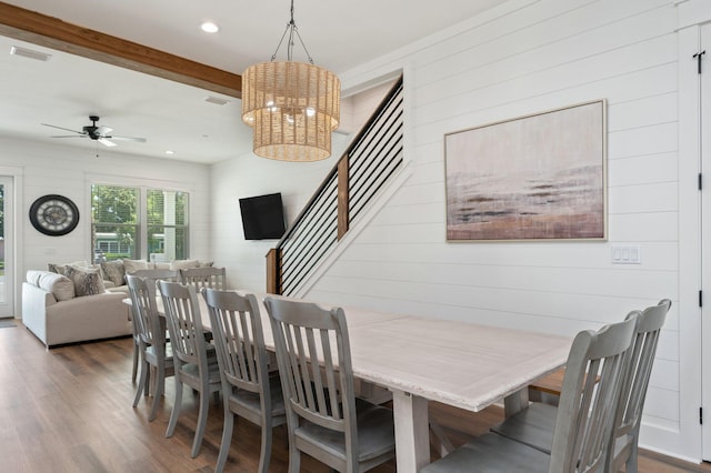 dining space featuring ceiling fan with notable chandelier, beam ceiling, dark hardwood / wood-style flooring, and wooden walls