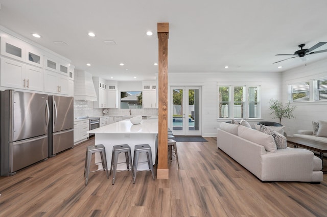 kitchen with white cabinets, dark hardwood / wood-style floors, appliances with stainless steel finishes, a kitchen bar, and custom range hood