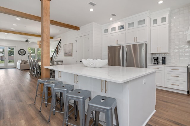 kitchen with ceiling fan, stainless steel fridge, a kitchen island, and white cabinetry