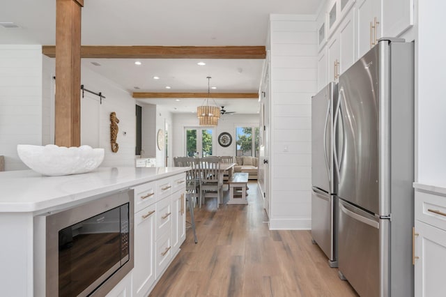 kitchen with a barn door, white cabinetry, hanging light fixtures, and stainless steel appliances