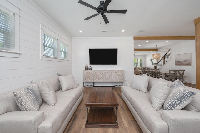 living room with hardwood / wood-style floors, ceiling fan with notable chandelier, and wood walls