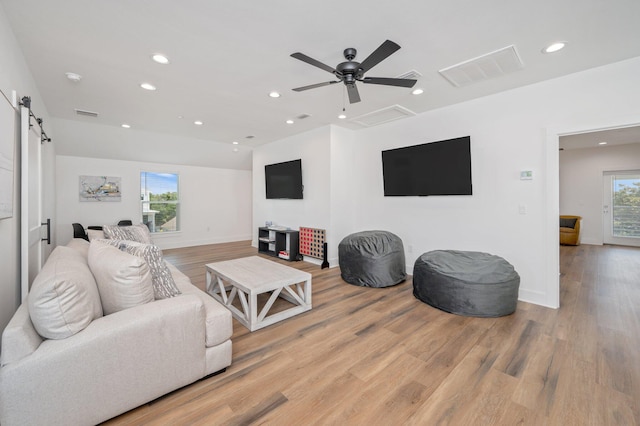 living room with ceiling fan, a barn door, and light wood-type flooring