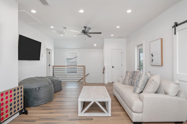 living room with a barn door, ceiling fan, and wood-type flooring