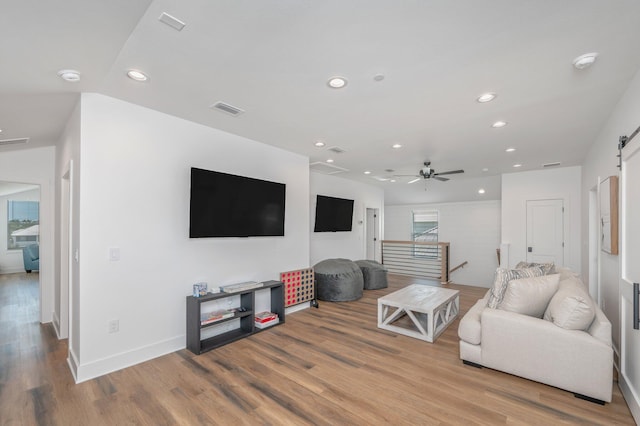 living room with a barn door, ceiling fan, and light hardwood / wood-style flooring