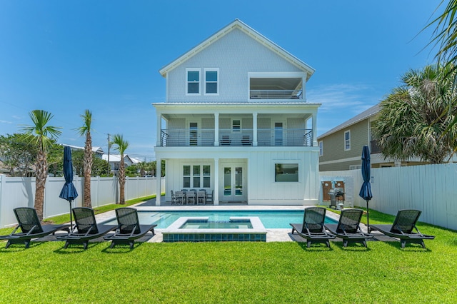 rear view of house featuring french doors, a yard, a balcony, and a pool with hot tub