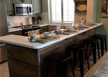 kitchen with gray cabinetry, range, backsplash, a kitchen bar, and light tile floors