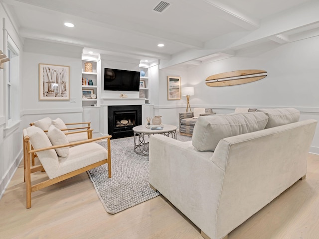 living room featuring built in shelves, hardwood / wood-style floors, and beamed ceiling