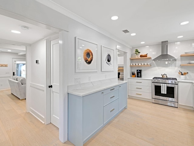 kitchen featuring backsplash, white cabinets, wall chimney range hood, stainless steel stove, and light wood-type flooring