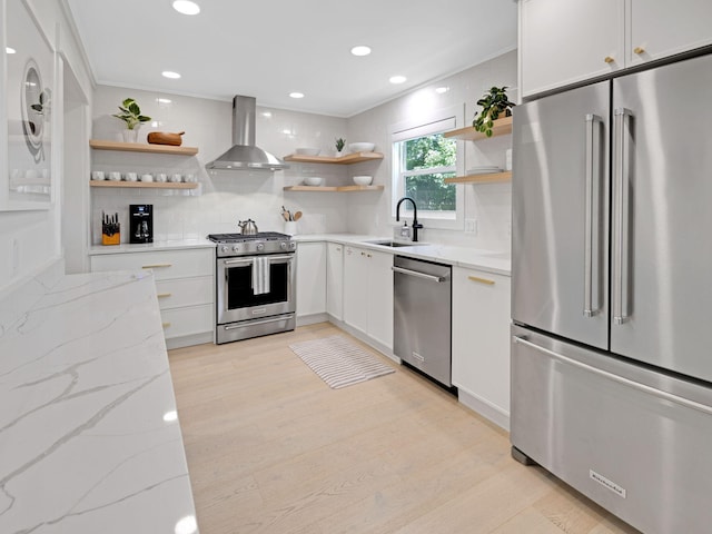 kitchen featuring white cabinets, high quality appliances, wall chimney exhaust hood, and light stone countertops