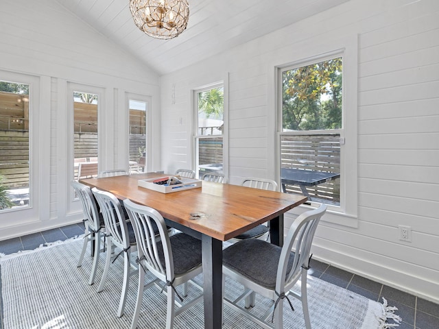 tiled dining space with wooden walls, plenty of natural light, vaulted ceiling, and an inviting chandelier