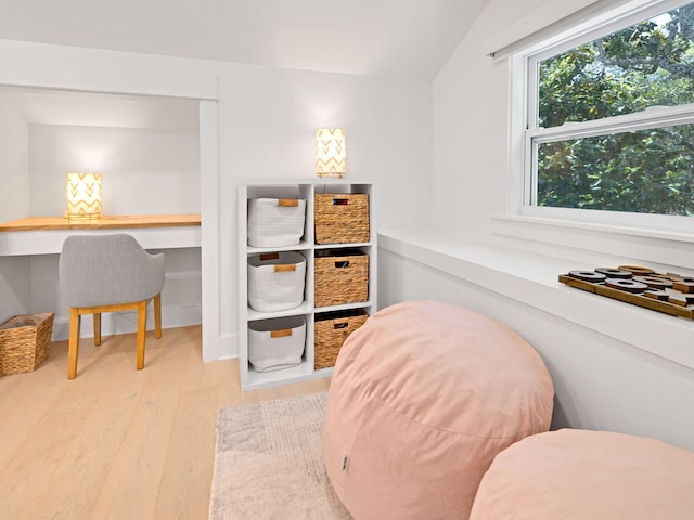 interior space with lofted ceiling, built in desk, and light hardwood / wood-style flooring