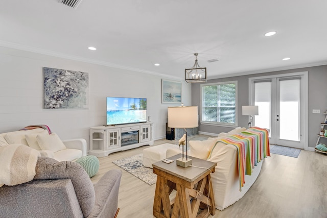 living room featuring french doors, light hardwood / wood-style floors, an inviting chandelier, and crown molding