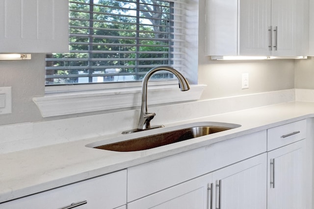 interior details with light stone counters, white cabinetry, and sink