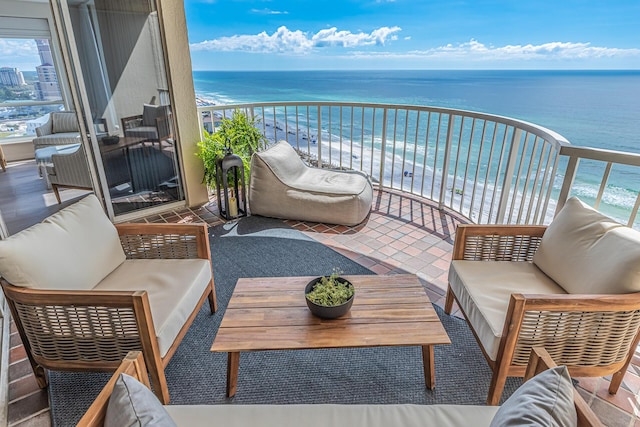 balcony with an outdoor living space, a water view, and a beach view