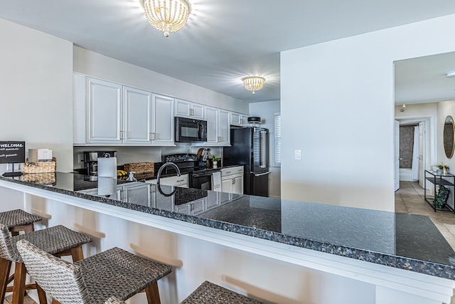 kitchen with black appliances, a kitchen breakfast bar, white cabinetry, and kitchen peninsula