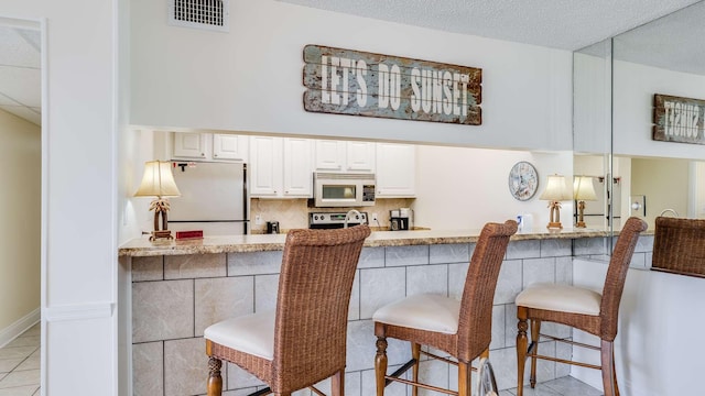 kitchen with a breakfast bar, appliances with stainless steel finishes, tasteful backsplash, a textured ceiling, and light tile patterned flooring