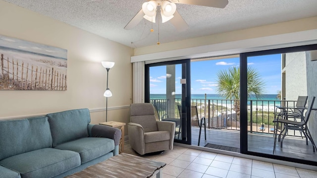 tiled living room featuring a water view, ceiling fan, plenty of natural light, and a textured ceiling