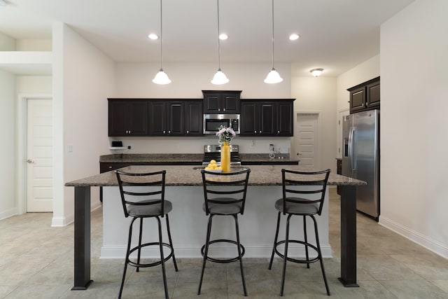 kitchen featuring a breakfast bar, dark stone countertops, an island with sink, pendant lighting, and stainless steel appliances