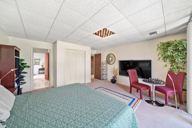 carpeted bedroom featuring a drop ceiling and a closet