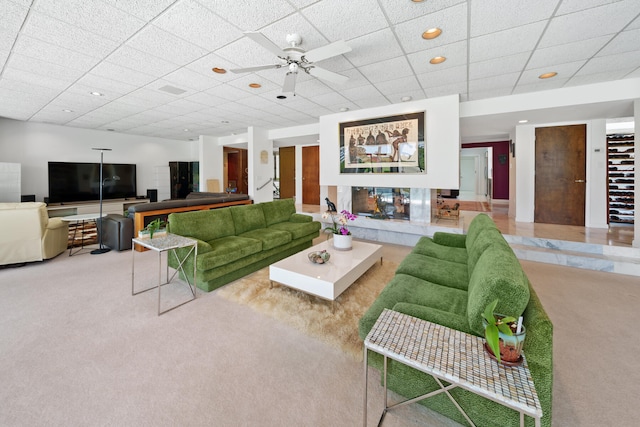 carpeted living room featuring ceiling fan and a drop ceiling