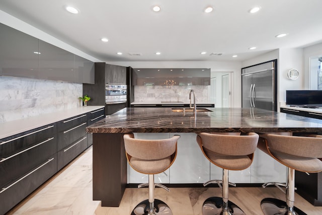 kitchen with sink, stainless steel appliances, tasteful backsplash, a breakfast bar area, and a center island with sink