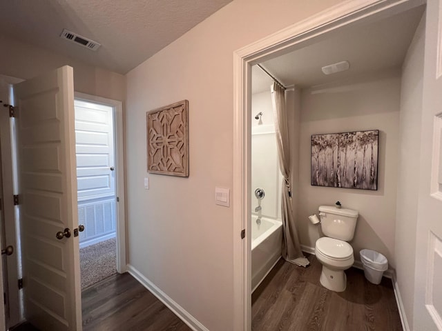 bathroom with hardwood / wood-style floors, toilet, shower / tub combination, and a textured ceiling