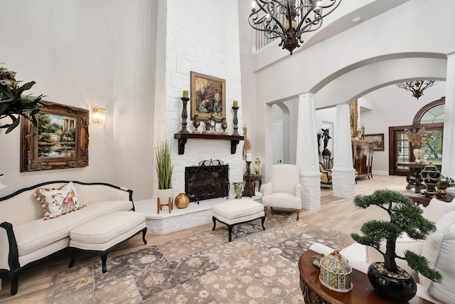 living area with arched walkways, a stone fireplace, wood finished floors, and a towering ceiling