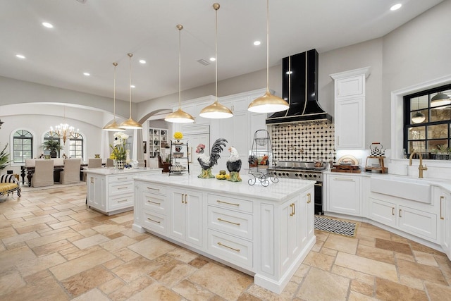 kitchen featuring arched walkways, range with two ovens, wall chimney exhaust hood, a kitchen island, and stone tile flooring