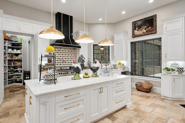 kitchen featuring recessed lighting, white cabinets, wall chimney range hood, and stone tile floors