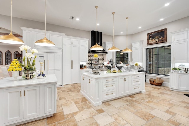 kitchen with visible vents, wall chimney exhaust hood, a kitchen island, stone tile flooring, and white cabinetry