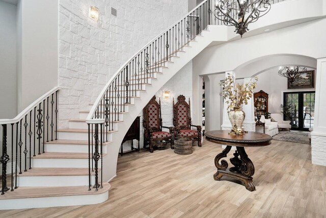 stairs featuring a towering ceiling, a chandelier, french doors, and light wood-type flooring