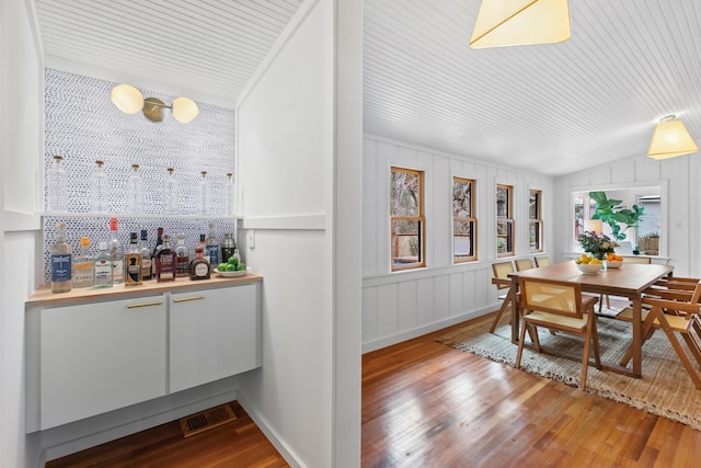 dining room with bar, light hardwood / wood-style floors, and vaulted ceiling