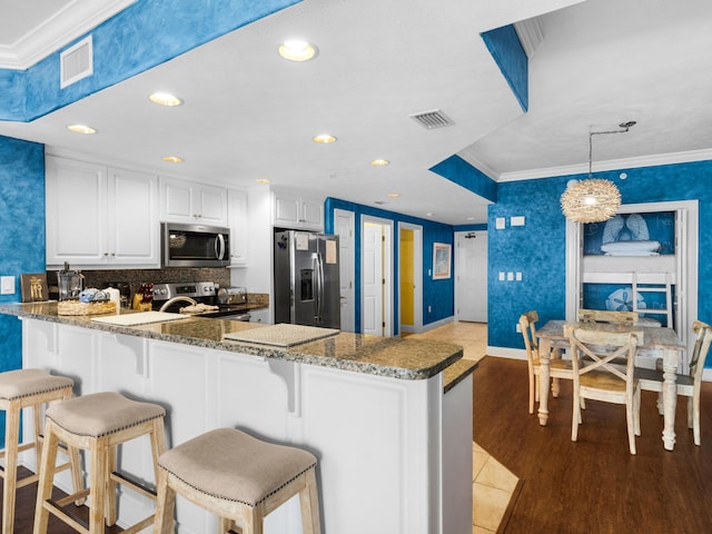 kitchen with hanging light fixtures, appliances with stainless steel finishes, white cabinets, kitchen peninsula, and wood-type flooring