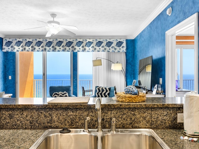 kitchen with a water view, ceiling fan, crown molding, sink, and a textured ceiling