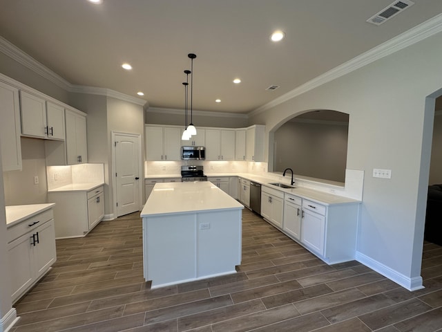 kitchen featuring stainless steel appliances, dark wood-type flooring, sink, a center island, and white cabinetry