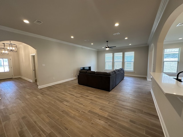 living room with ceiling fan with notable chandelier, ornamental molding, and dark wood-type flooring