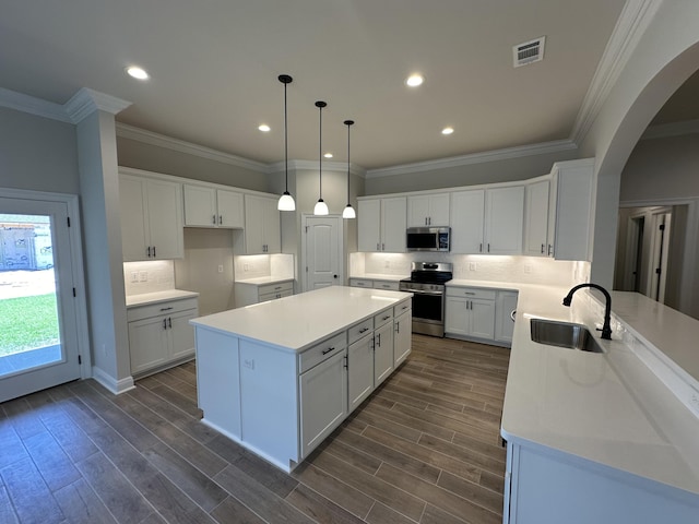 kitchen featuring appliances with stainless steel finishes, a kitchen island, sink, white cabinetry, and hanging light fixtures