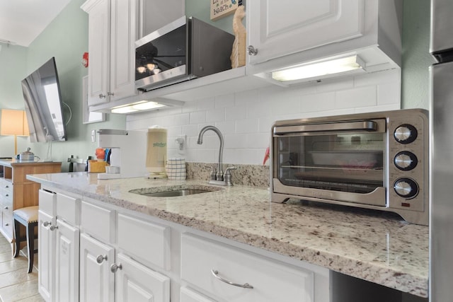 kitchen with white cabinets, light stone counters, backsplash, sink, and light tile floors