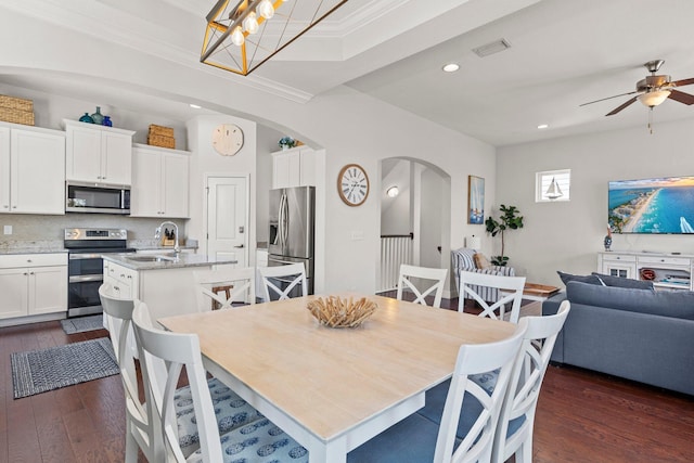 dining space featuring crown molding, sink, dark wood-type flooring, and ceiling fan with notable chandelier