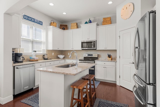 kitchen with light stone countertops, stainless steel appliances, dark wood-type flooring, a center island with sink, and white cabinetry