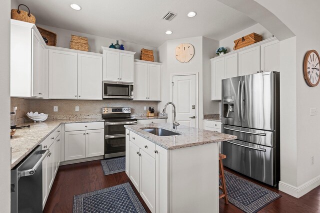 kitchen with light stone countertops, appliances with stainless steel finishes, sink, white cabinets, and an island with sink
